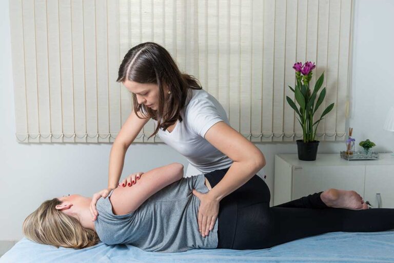 Patient in comfortable clothing discussing symptoms with a chiropractor beside an examination table.